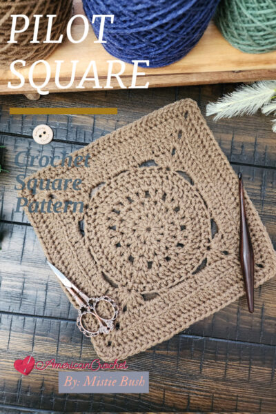 The Pilot Square crochet pattern displayed on a rustic wooden surface with a crochet hook, vintage scissors, and greenery. This 9-inch textured afghan block features a mix of single crochet, half double crochet, double crochet, treble crochet, back loop only stitches, and V-stitches, making it a beautifully balanced design for blankets and home décor