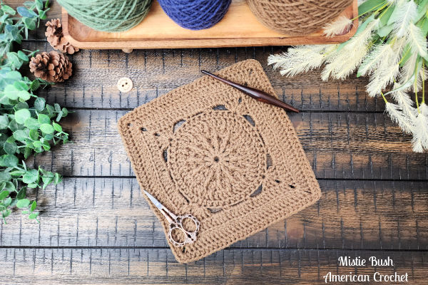 Durst Square crochet block styled with a wooden crochet hook and ornate scissors, showcasing the structured texture created by post stitches and back loop techniques on a rustic wooden background.