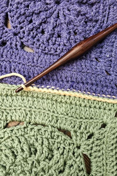 Close-up of a partially completed single crochet seam between two textured crochet squares.