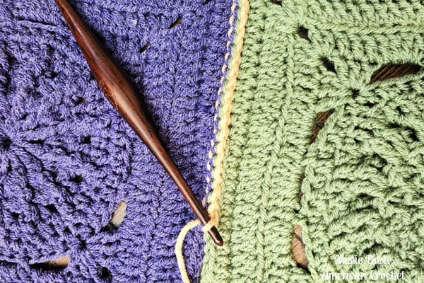 Close-up of a partially completed single crochet seam between two textured crochet squares.