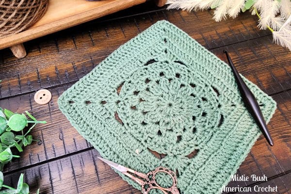 Overhead view of the Enclave Square showing structured rounds and clustered stitches, crocheted in soft green yarn with a wood background.